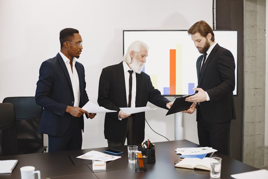 Three businessmen discussing documents in a conference setting with a presentation screen